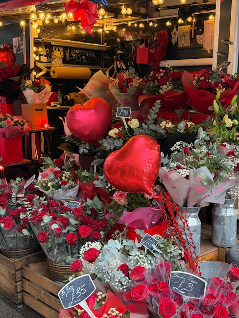 A vibrant display of fresh flowers at a florist shop, featuring a variety of red and white roses, white baby's breath, and greenery arranged in bouquets and wrapping paper. Prominent in the arrangemen